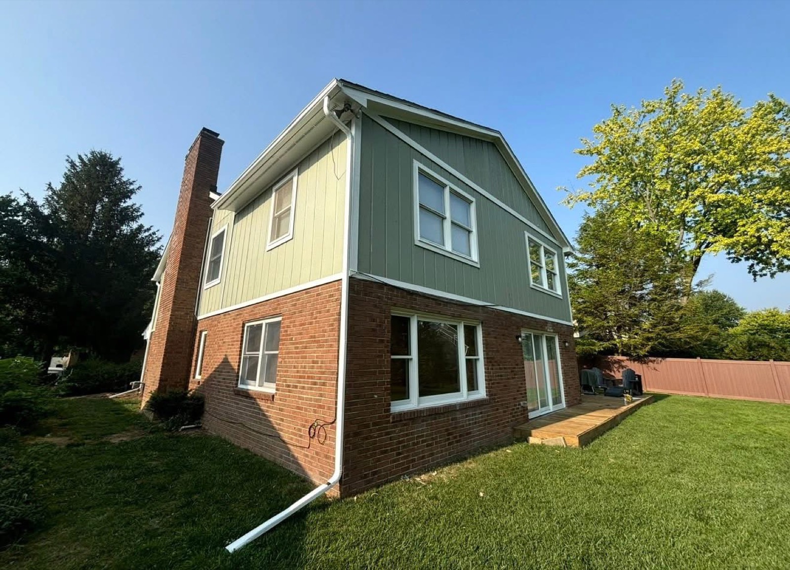 Two-story home with freshly painted green board-and-batten upper siding above a red brick lower level and white window trim