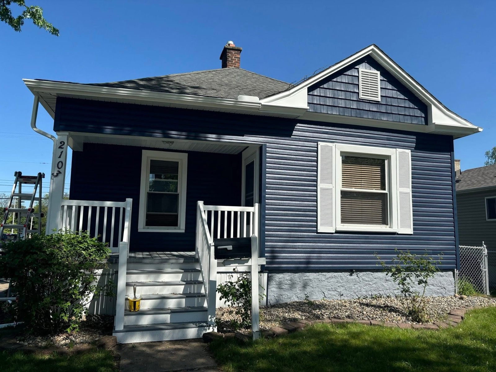 Single-story bungalow with fresh navy blue lap siding, white trim, a white porch railing, and blue shake shingles in the gable
