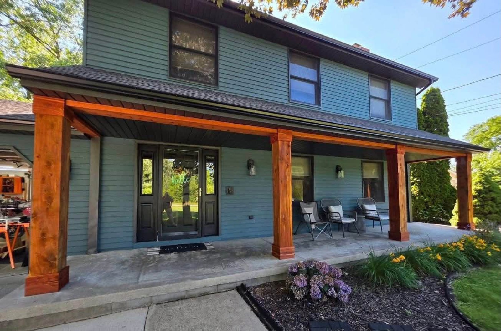 Two-story home painted teal-blue with black-trimmed windows and a covered front porch with natural-stained wood posts and beams