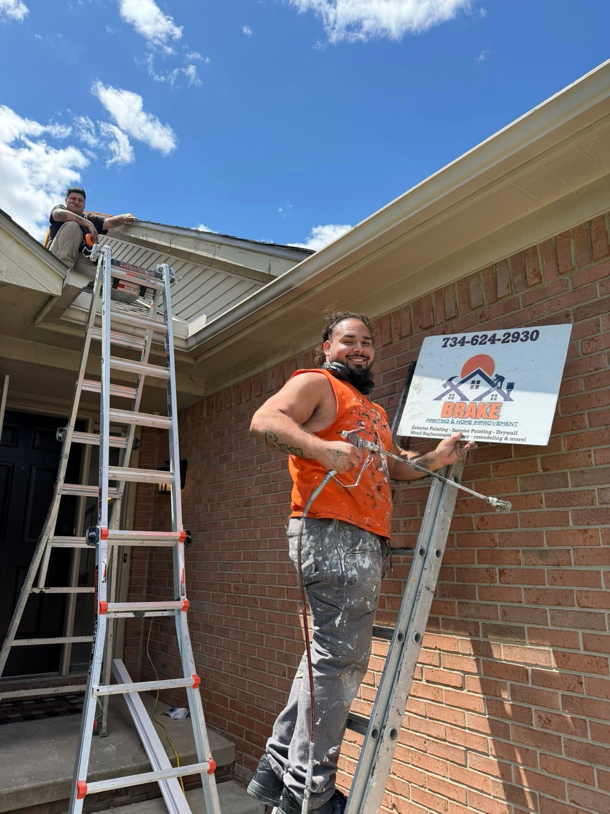 Two Brake crew members working on the gutters, soffit, and trim of a brick home from ladders