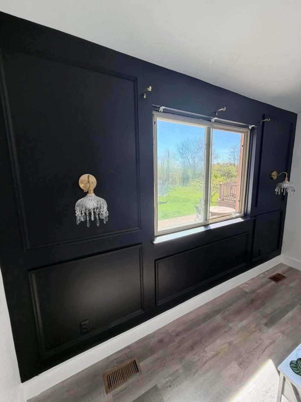 Interior accent wall painted matte black with picture-frame panel molding, brass wall sconces, and a white-trimmed window
