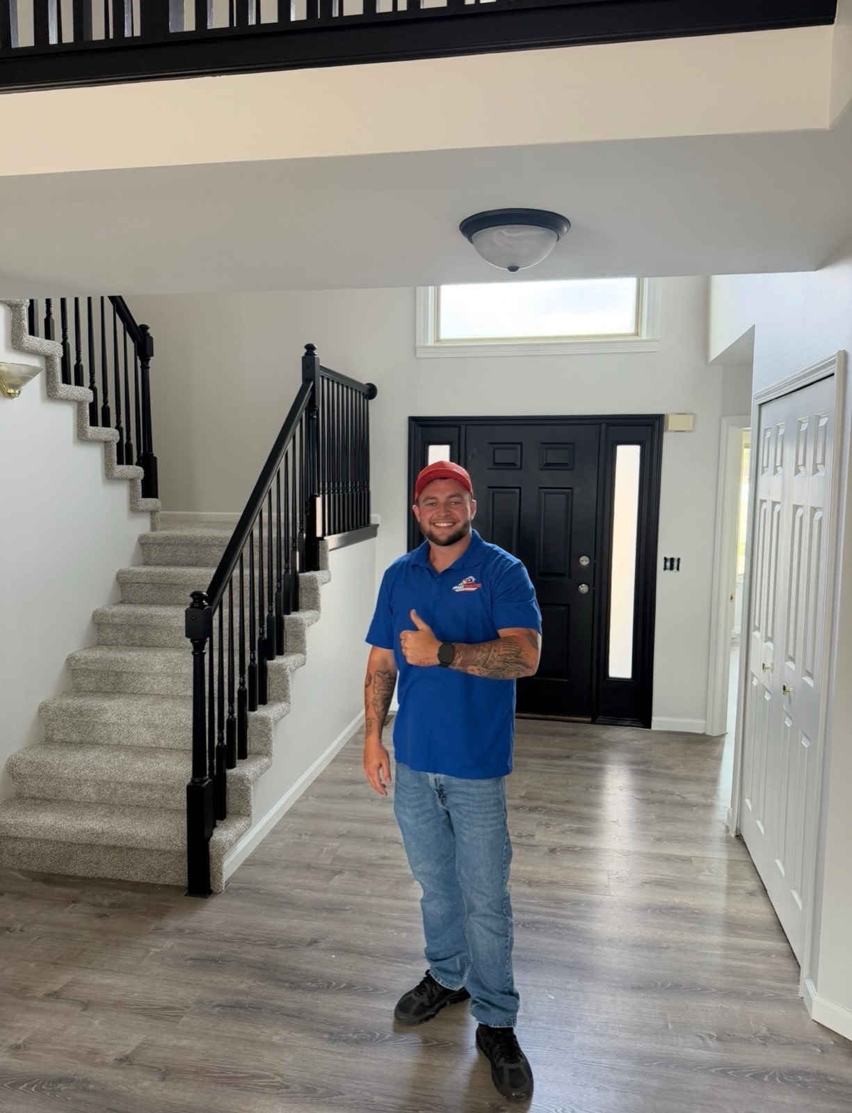 Interior entryway with a black-painted staircase railing, black front door, and gray wood-look floors, with a Brake crew member giving a thumbs up