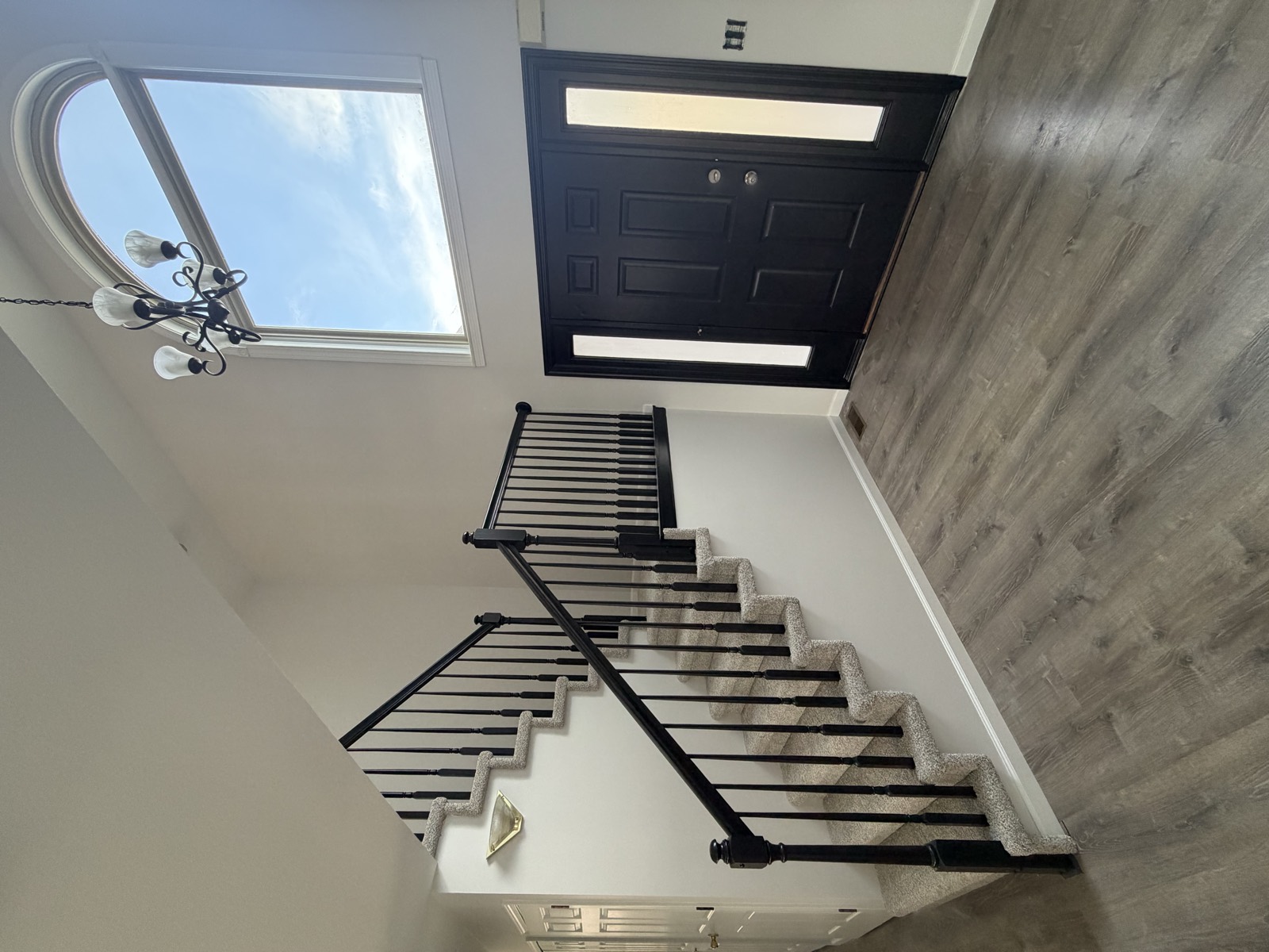 Two-story entry foyer with a black-painted staircase railing and balusters, a black front door with sidelight, an arched transom window, and gray wood-look floors